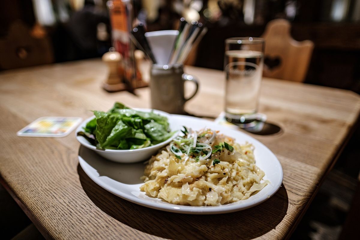 Teller mit Käsespätzle und Röstzwiebeln, daneben ein Salat